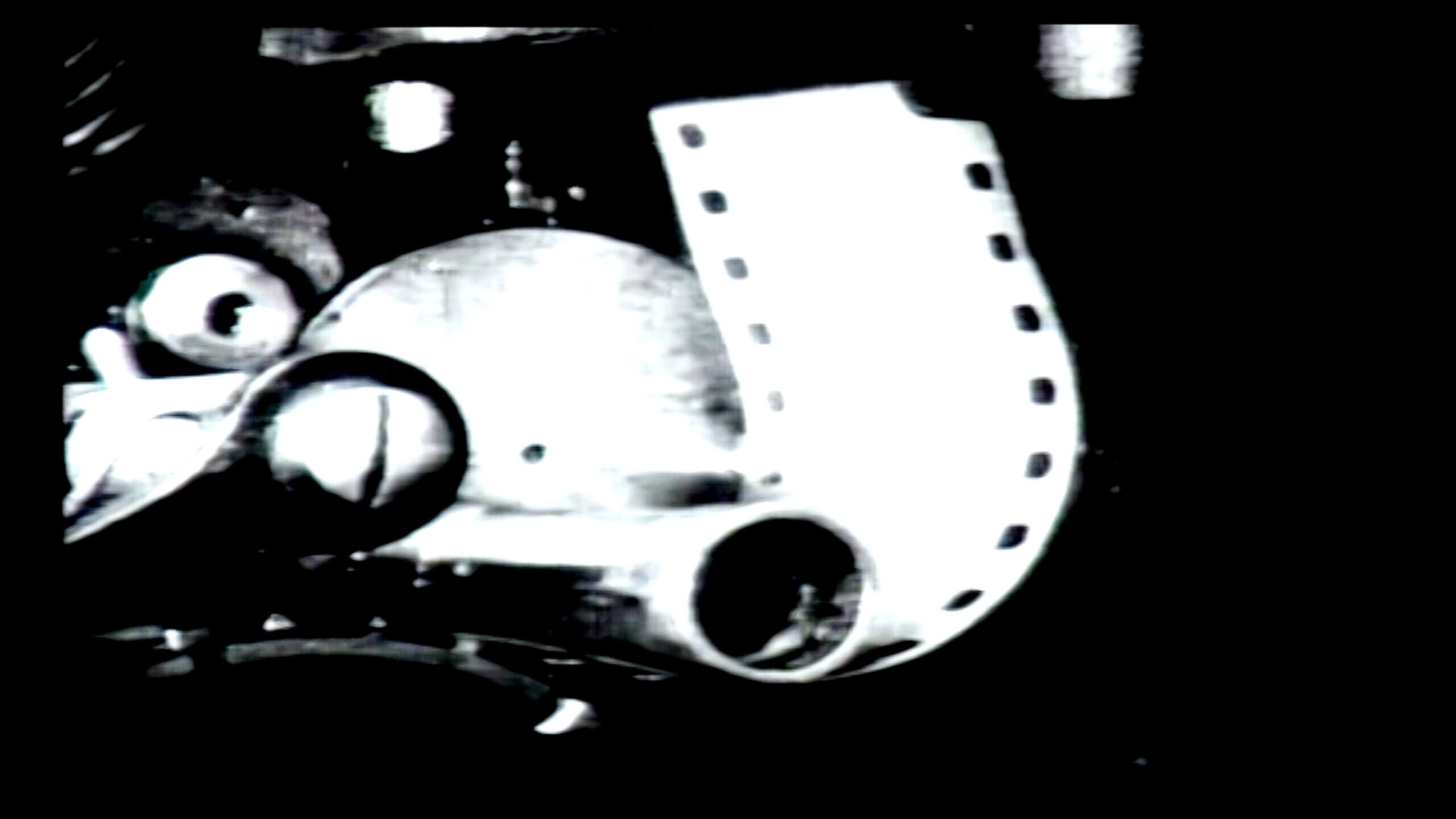 Image en noir et blanc d'un film pellicule entraîné dans le mécanisme d'un projecteur, tirée du film LE LIVRE D'IMAGE de Jean-Luc Godard