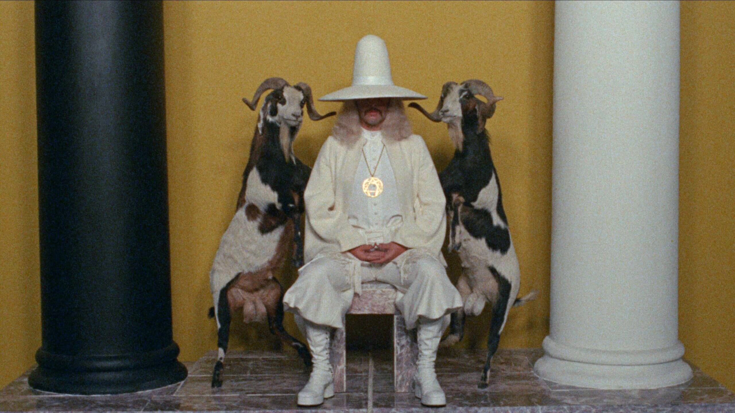 Un homme chapeauté trône entre deux chèvres dans une scène du film La montagne sacrée