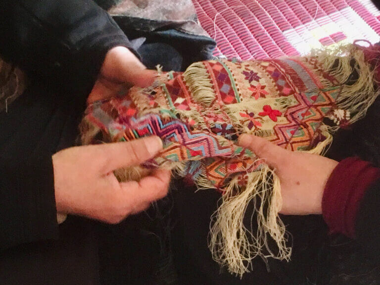 Des mains de femmes palestiniennes à l'ouvrage sur une broderie dans une scène du film Stitching Palestine.
