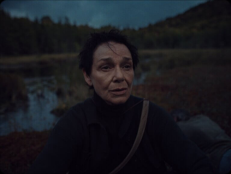 Au crépuscule, une femme d'âge moyen aux cheveux courts avec, à l'arrière-plan, un paysage marécageux.