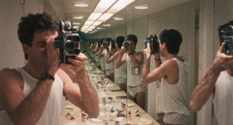 Dans une salle de bain recouvertes de miroirs sur trois côtés, un homme en sous-vêtements filme ses reflets.