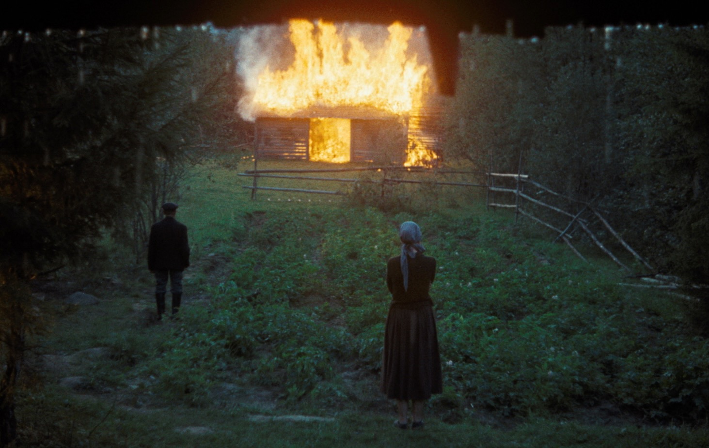 Un homme et une femme regardent une cabane brûler sous la pluie.
